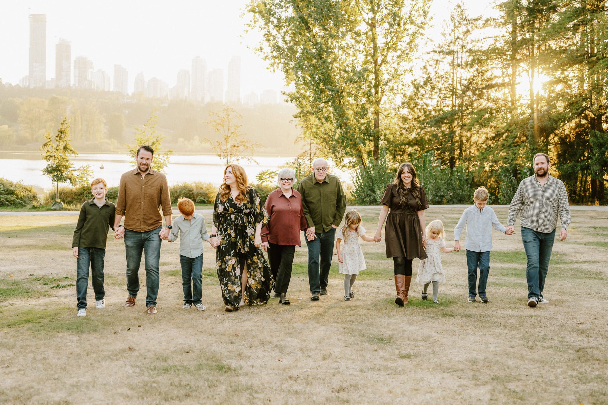 Urban family photos, extended family walking hand in hand through a park with the city skyline behind
