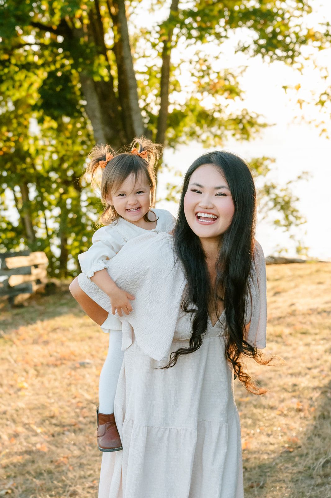Fun family pictures in a sunny park, mom laughing as she carries her little daughter
