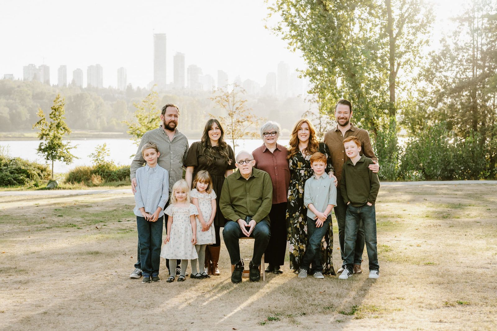 Family photography in Langley, extended family of three generations standing together in a park with the city skyline behind