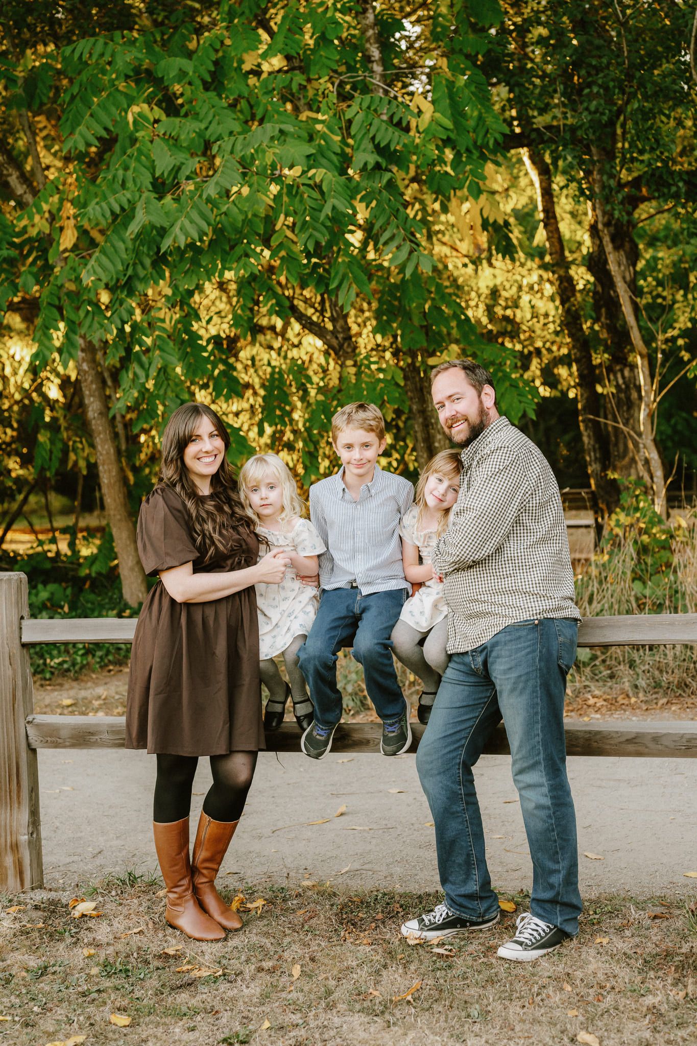Family photos in Langley, parents and their two children sitting on a wooden fence in the park
