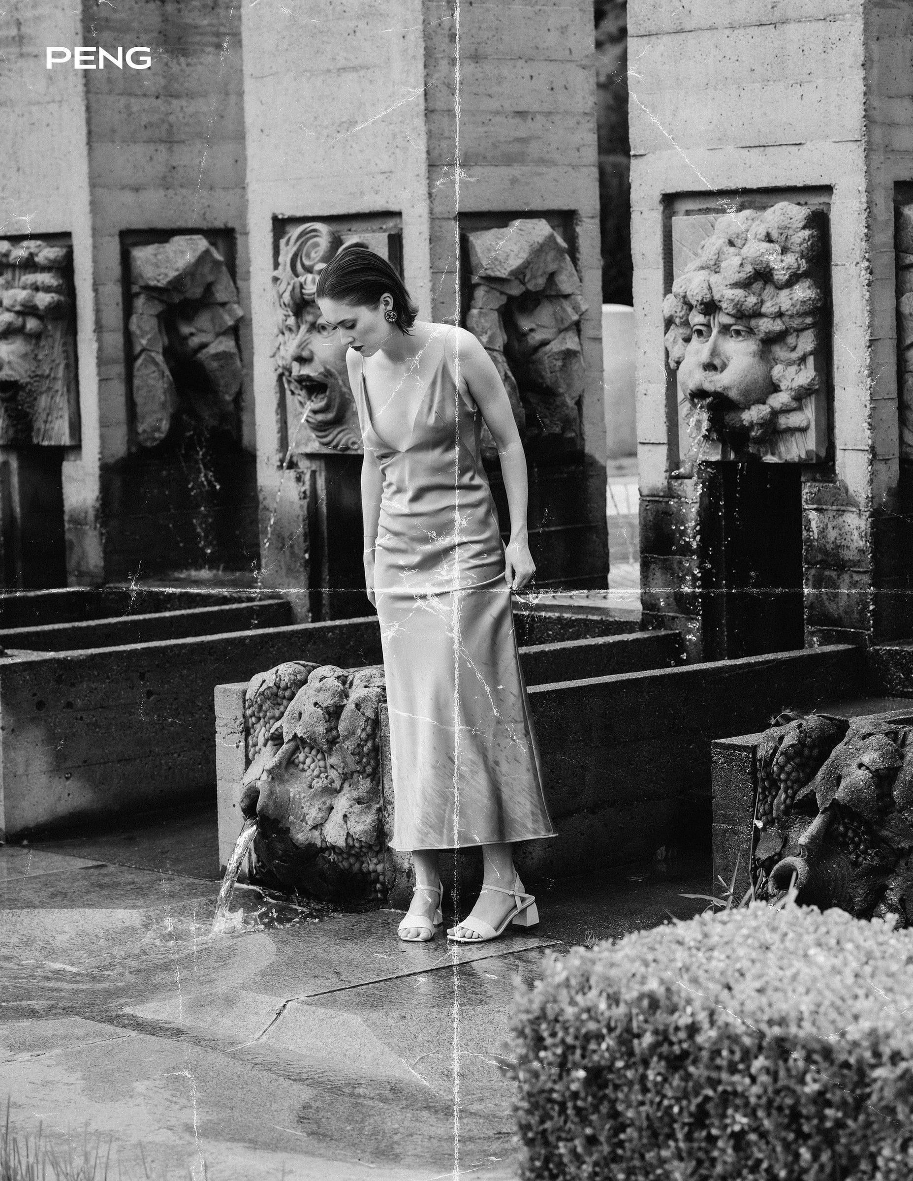 Black-and-white photo of a model in a white dress seated in a stone garden