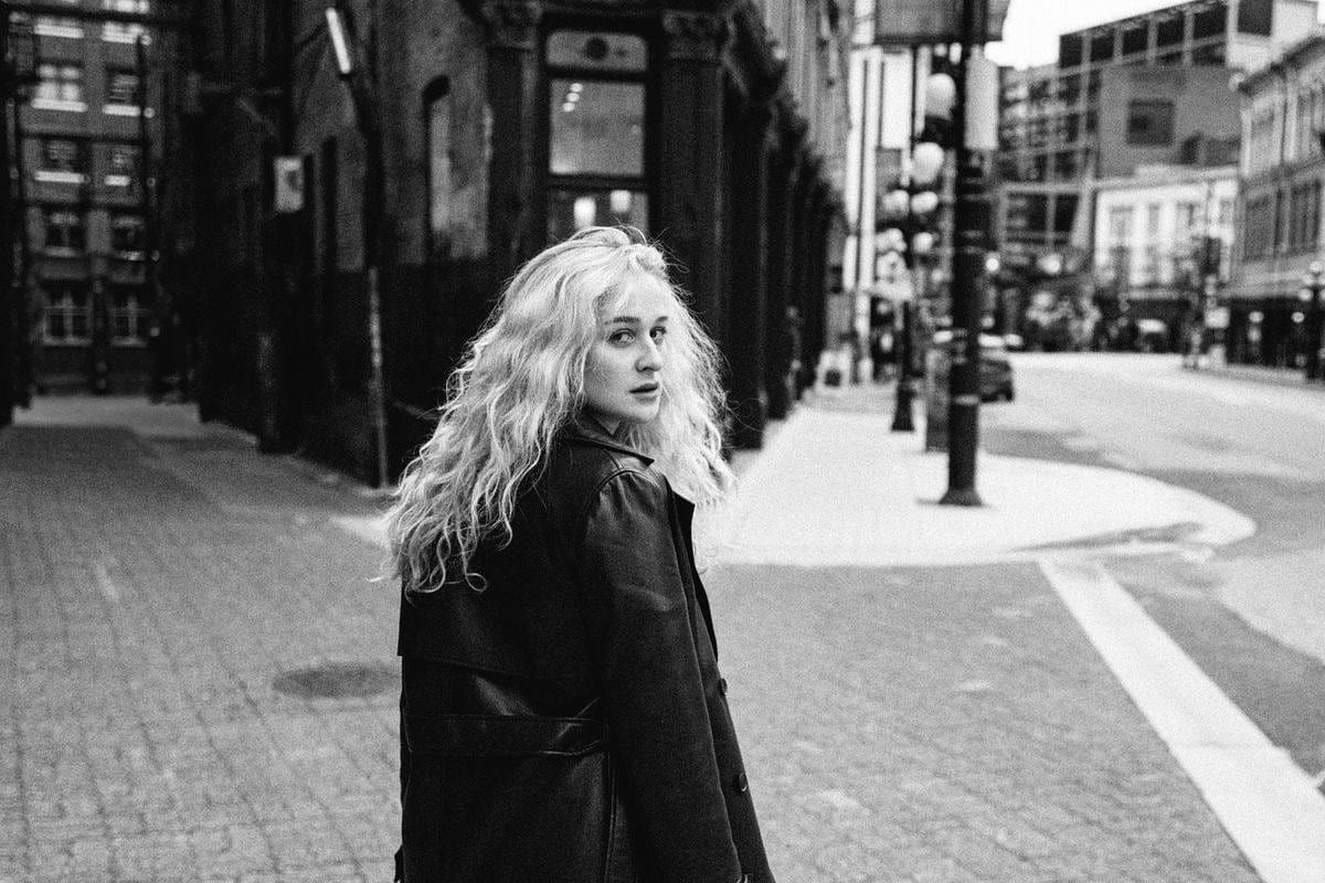 Black-and-white portrait of a blonde woman in a leather coat glancing back on a Gastown street