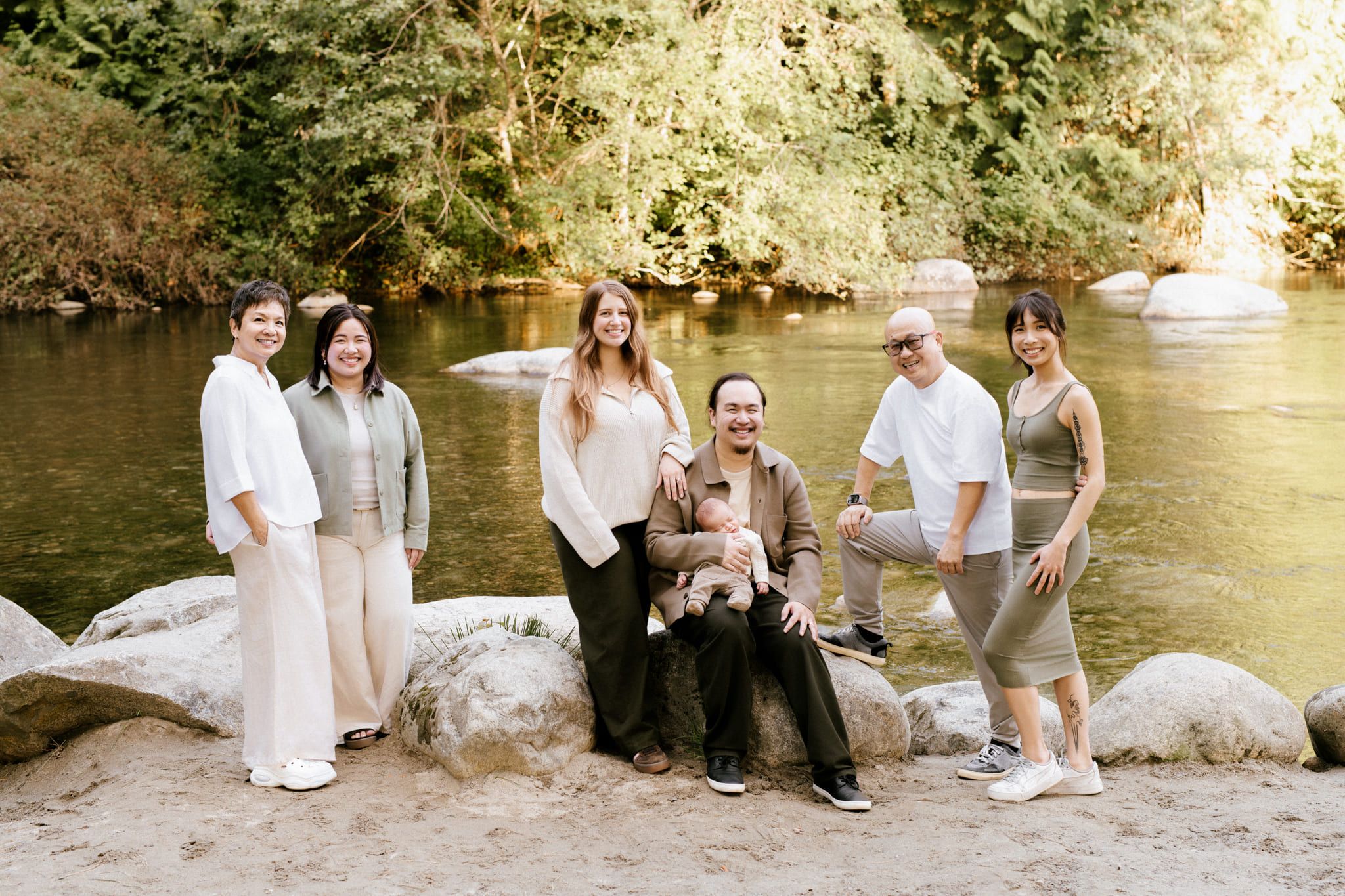 Family portrait photoshoot along a calm river bank in evening light, extended family standing on boulders