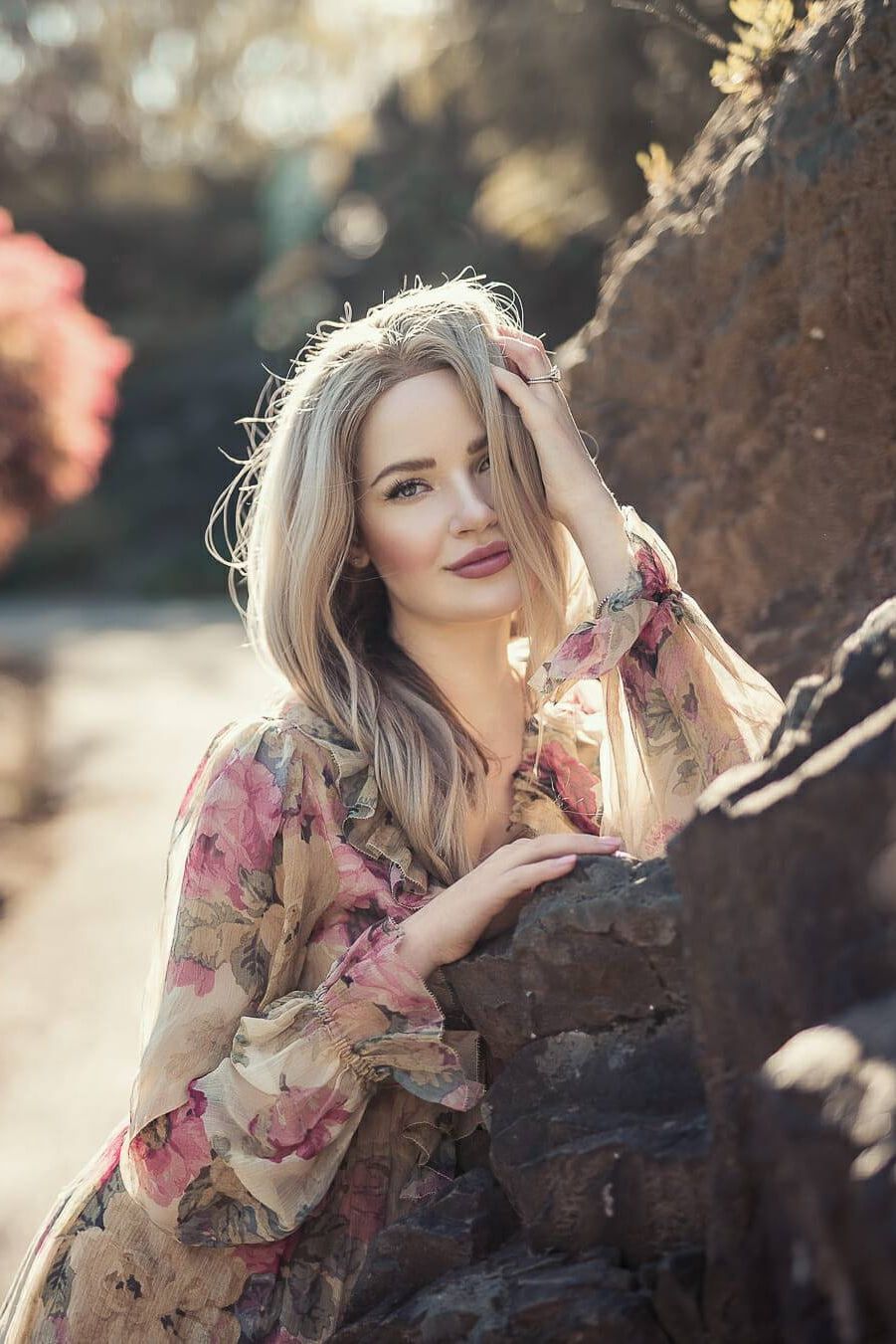 Professional portrait photography, woman in a floral dress leaning on a rock by a pond