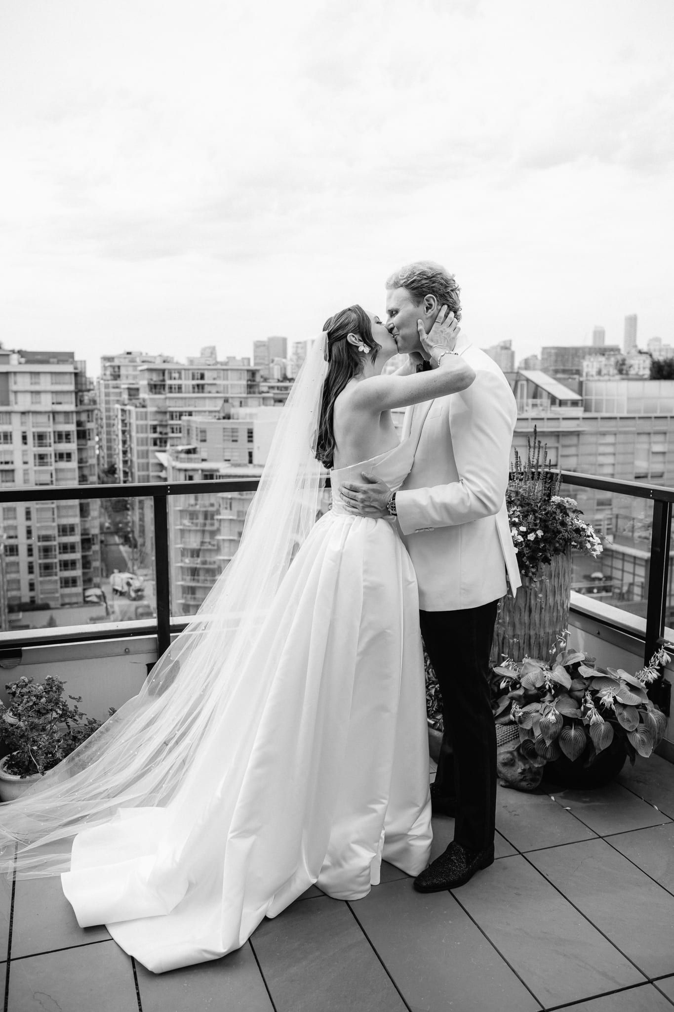 Bride photoshoot, black-and-white photo of the bride and groom kissing on a city rooftop