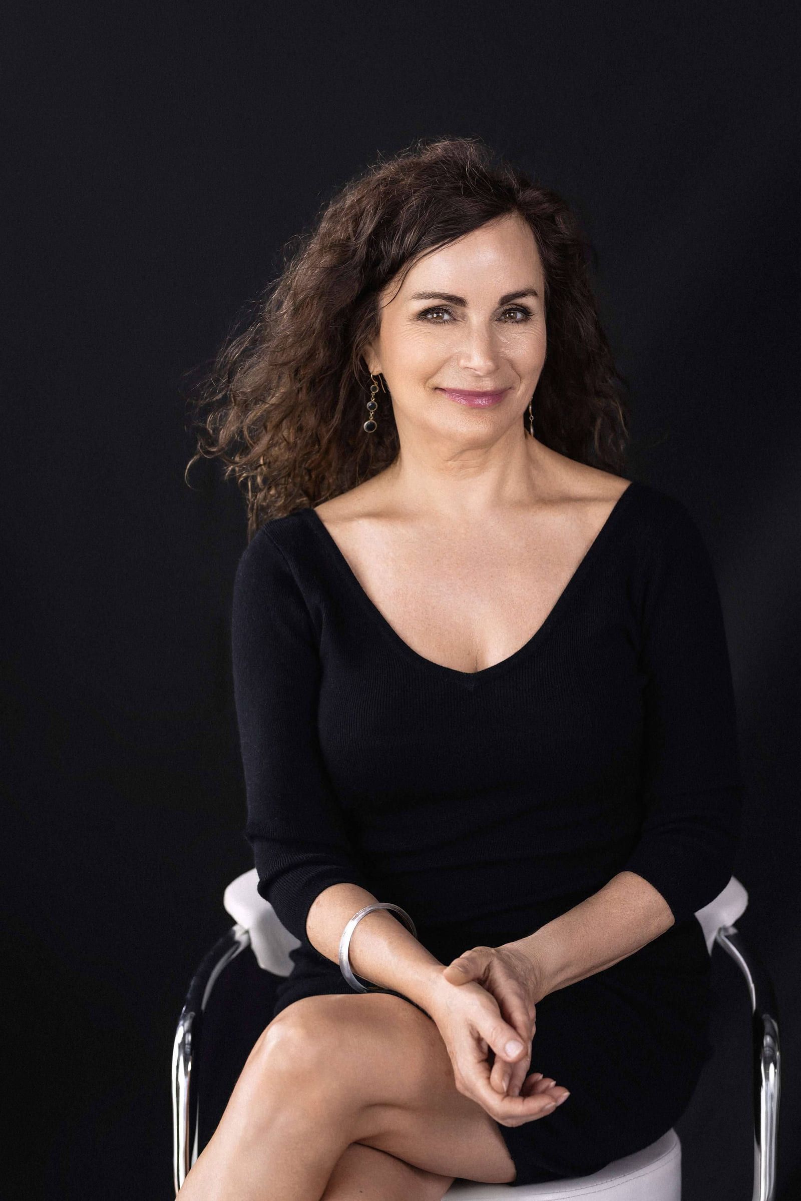 Woman in a black top seated on a stool, smiling