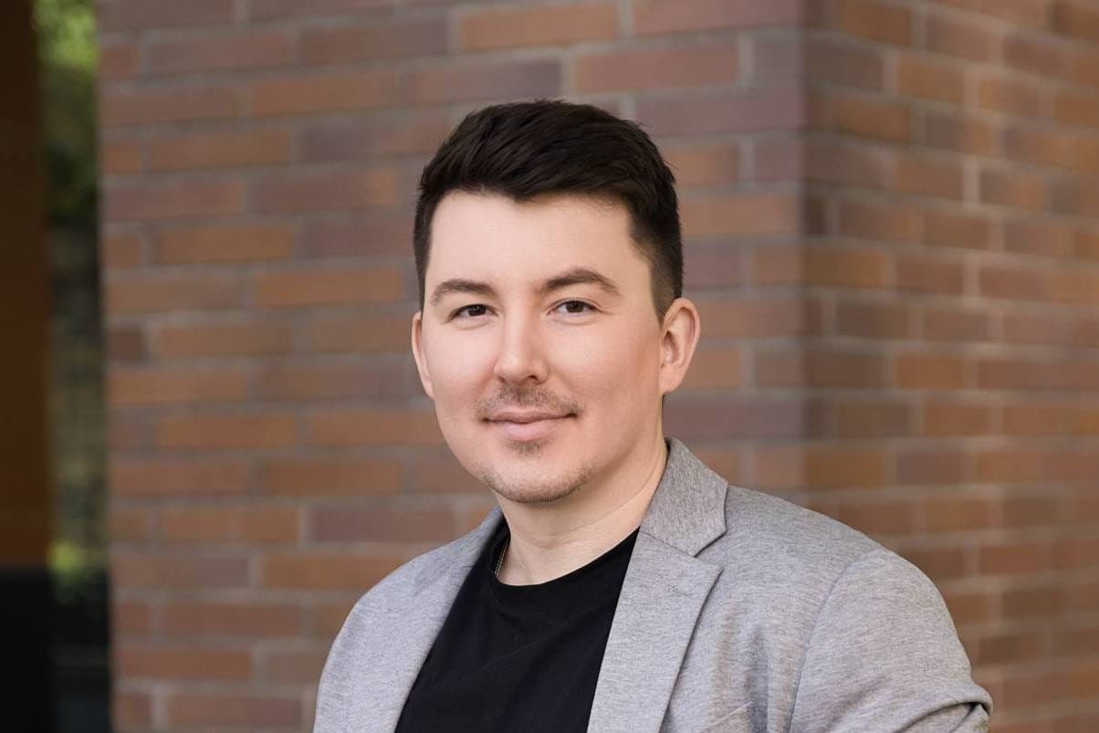 Outdoor headshot photos, smiling man in a grey blazer against a brick wall outdoors