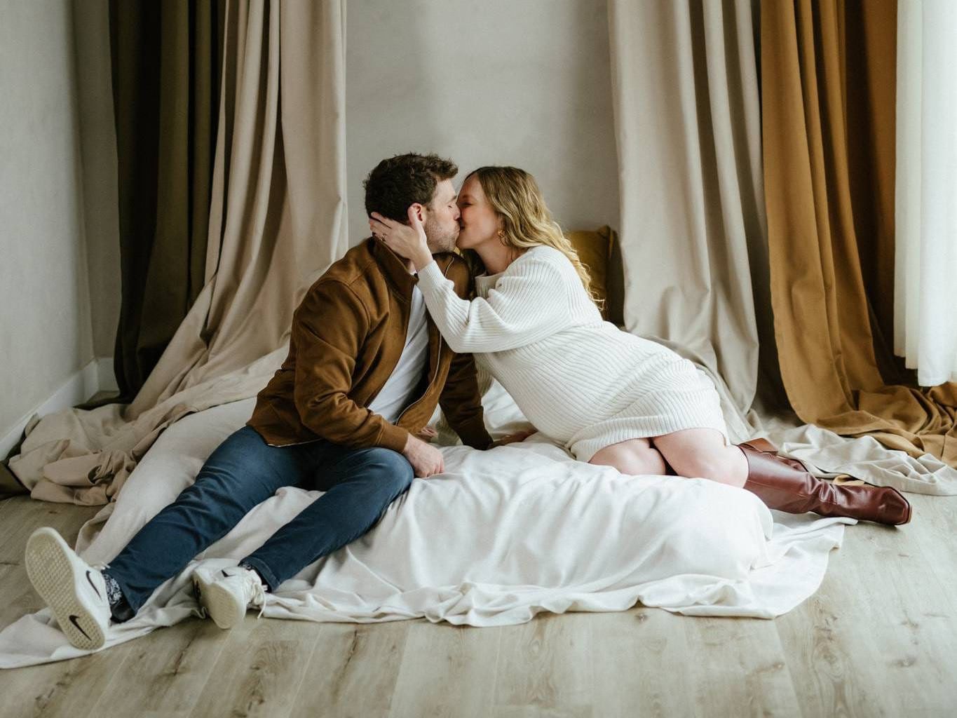 Couple photography studio session, couple kissing on a white bed between draped curtains in a studio