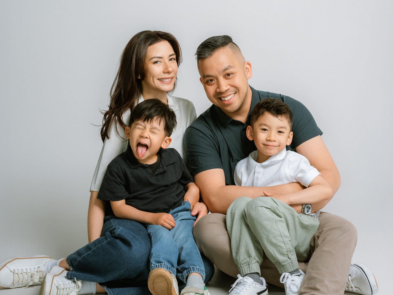 Family indoor photoshoot in a bright studio, parents laughing with their two boys