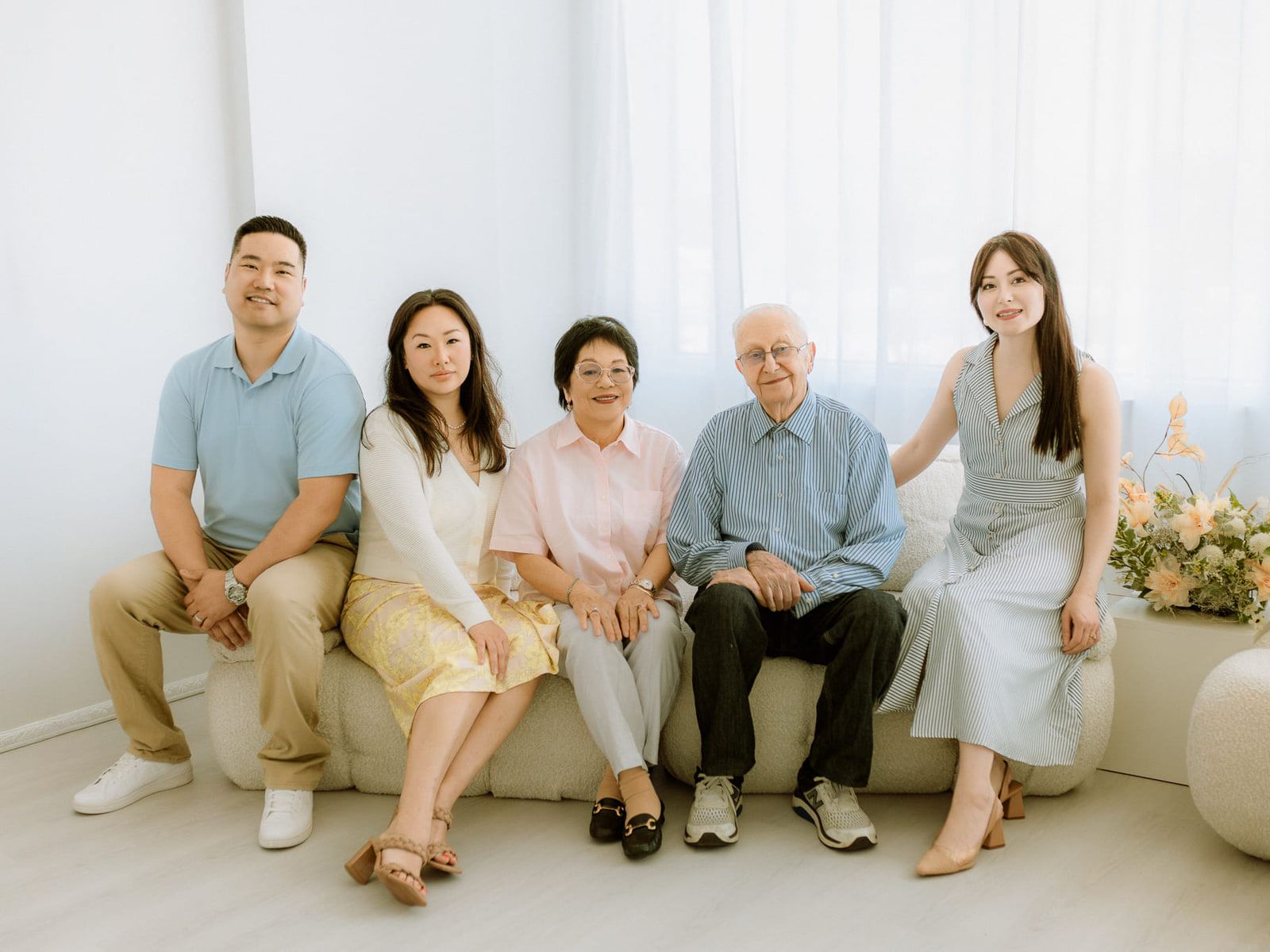 Indoor family photoshoot on a cream sofa in a bright studio, three generations sitting together