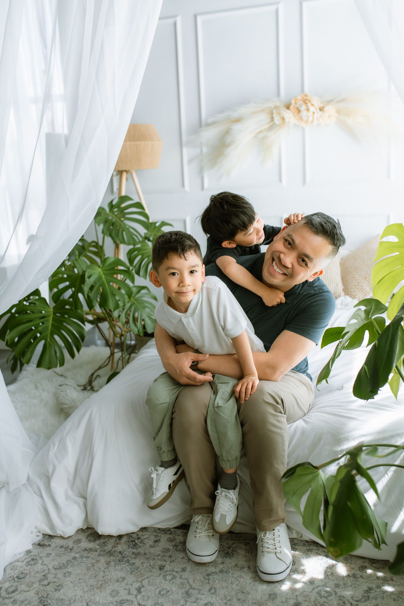 Indoor family photos, father and his boys laughing on a white studio bed among green plants