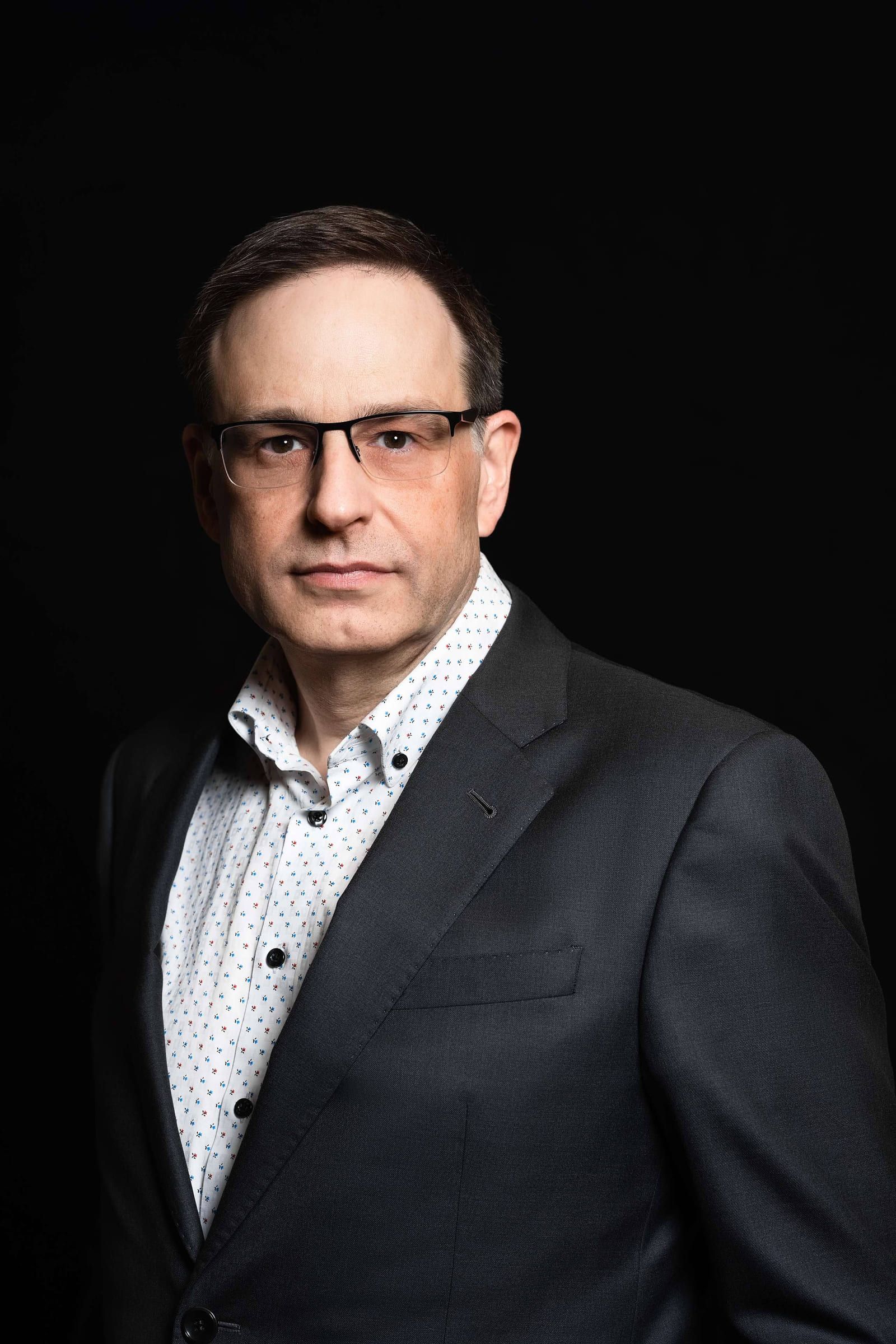 Business headshots photography on a black backdrop, man in glasses and a dark blazer, a business portrait