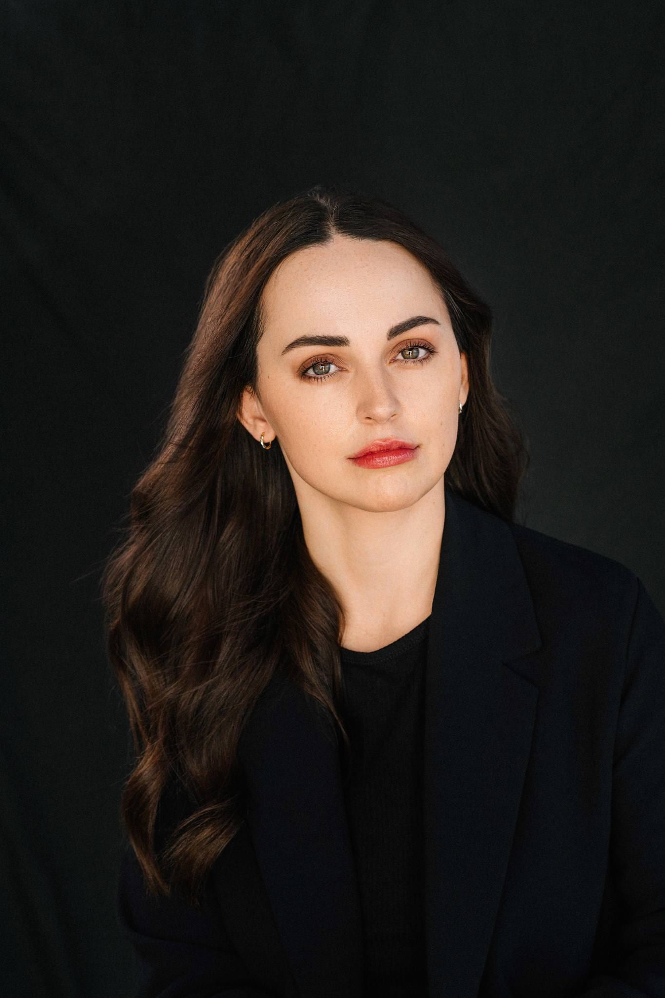 Professional corporate photoshoot on a dark backdrop, woman with long dark hair in a black blazer