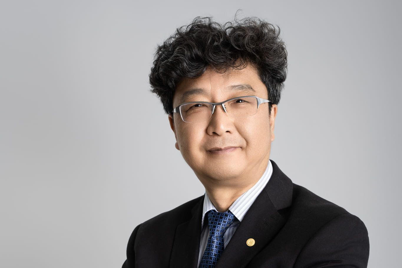 Corporate photo studio session, professional headshot of a man in glasses and a navy suit on a grey backdrop