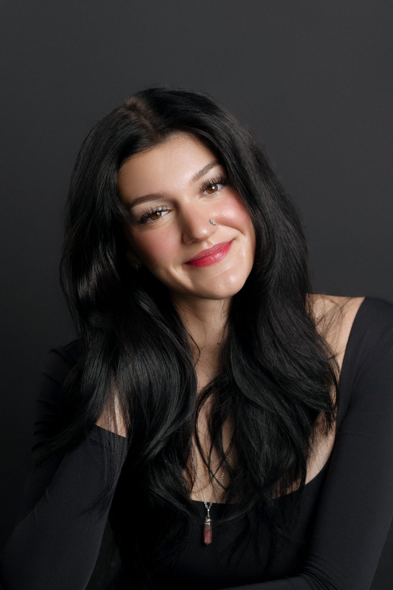 Headshot photo on a black backdrop, smiling young woman with long dark hair