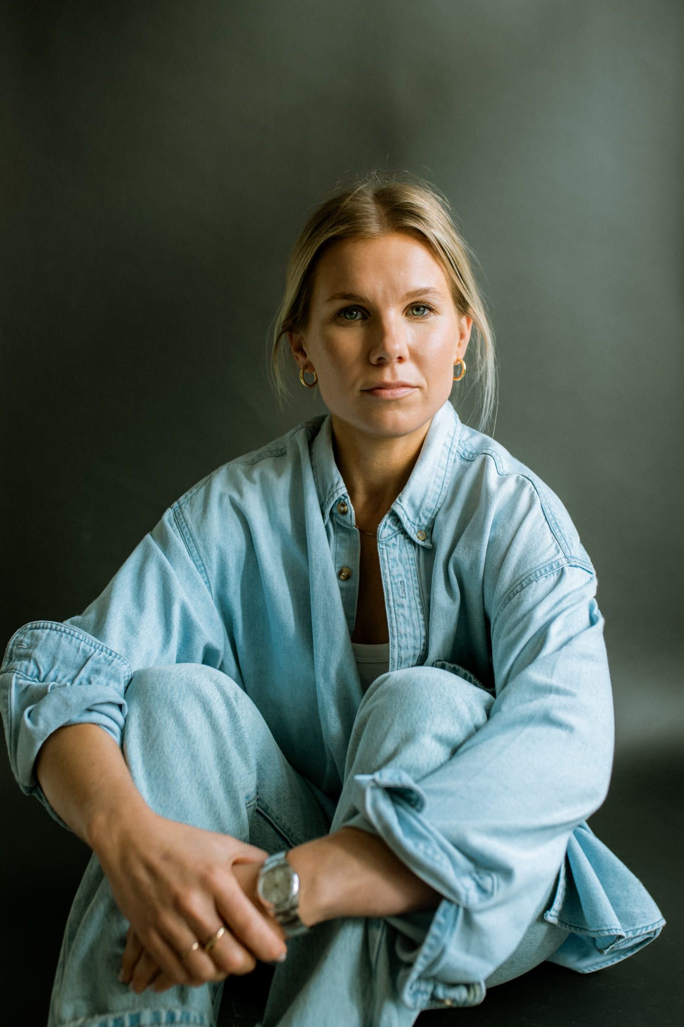 Studio headshot photography, woman in a denim shirt sitting cross-legged in a studio