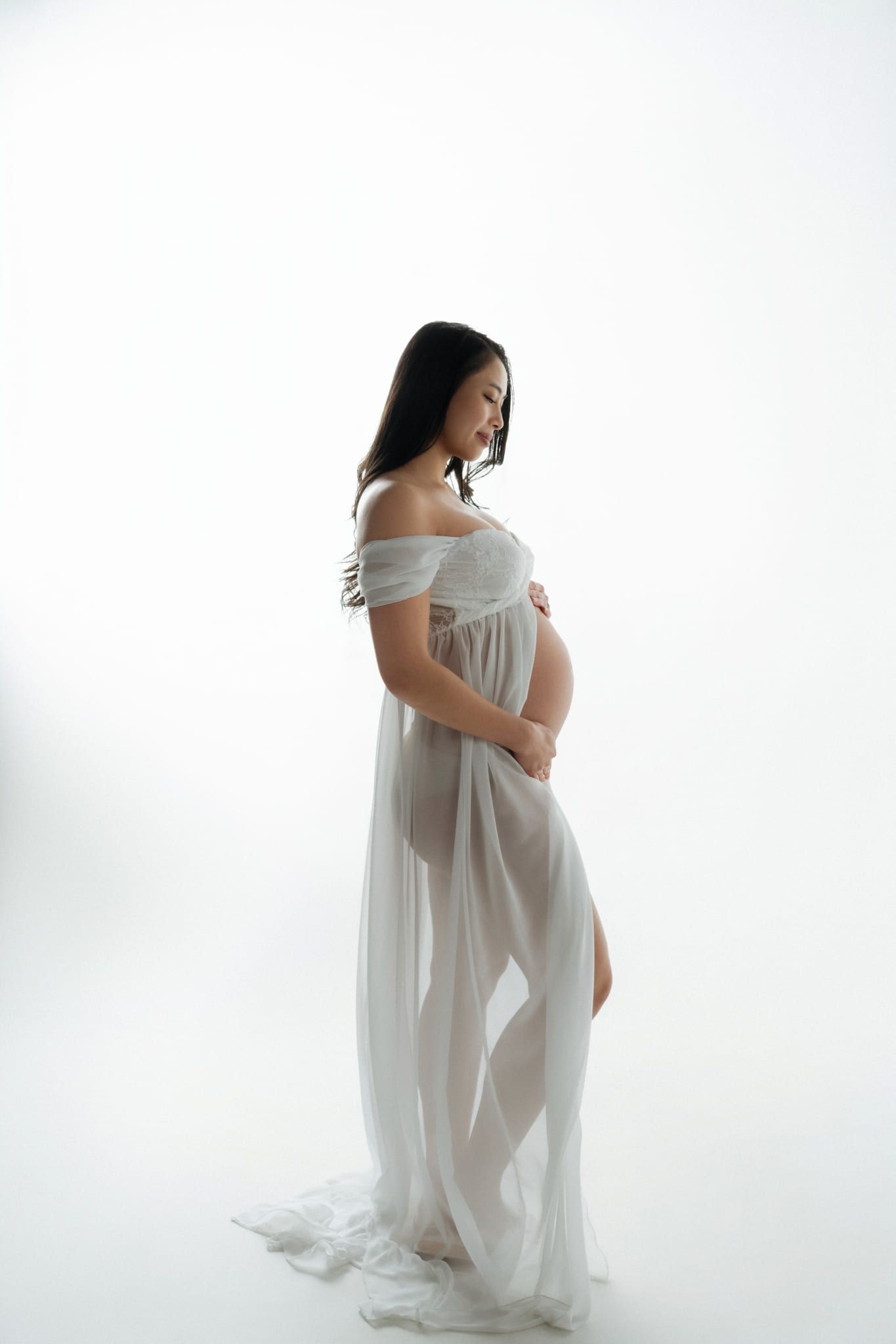 Black and white maternity photo in a bright studio, expectant mother in a sheer white gown