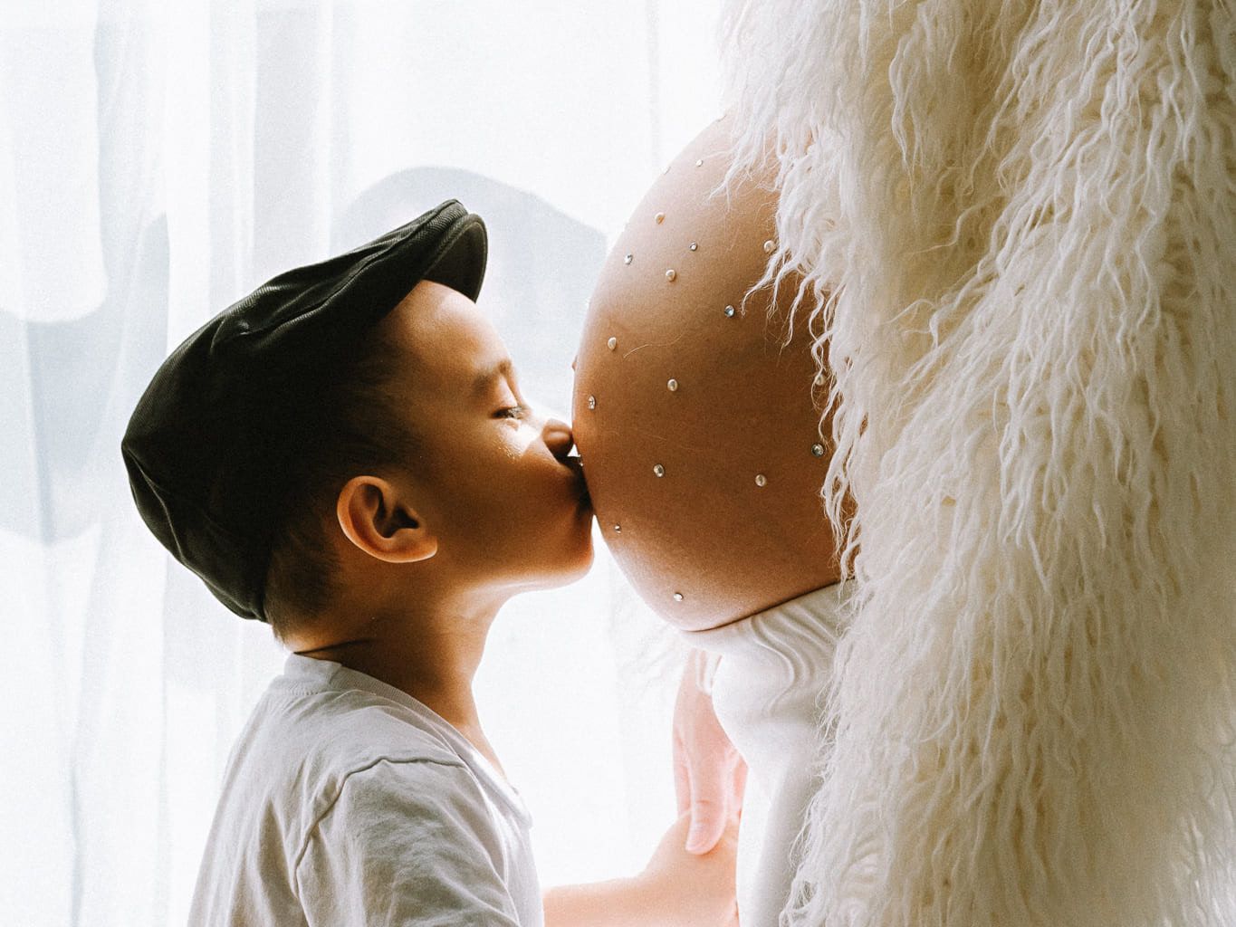 Maternity and family photography in a sunlit studio, little boy kissing his mother's bump