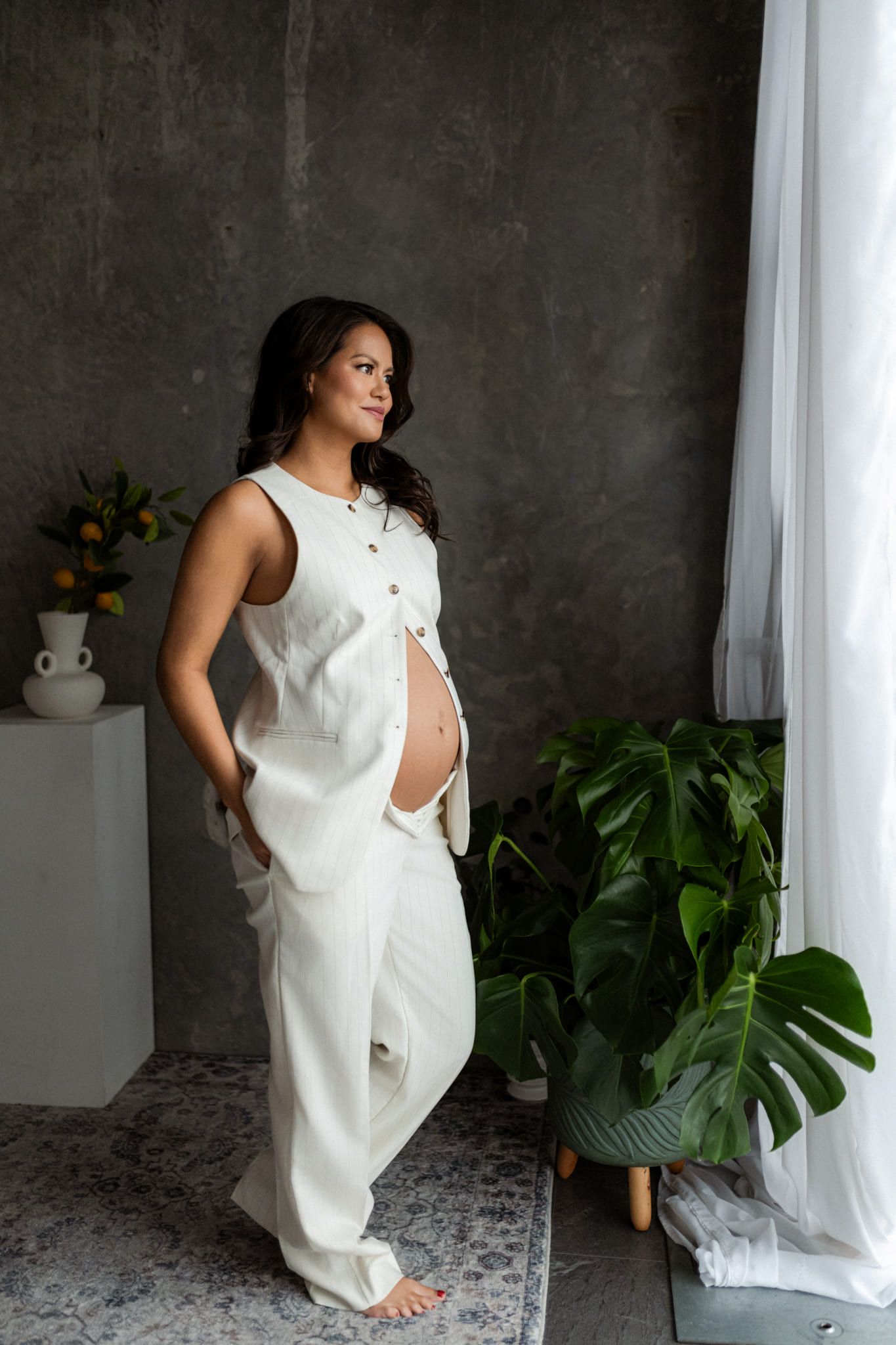 Maternity photoshoot, mom-to-be in white standing in a studio with plants