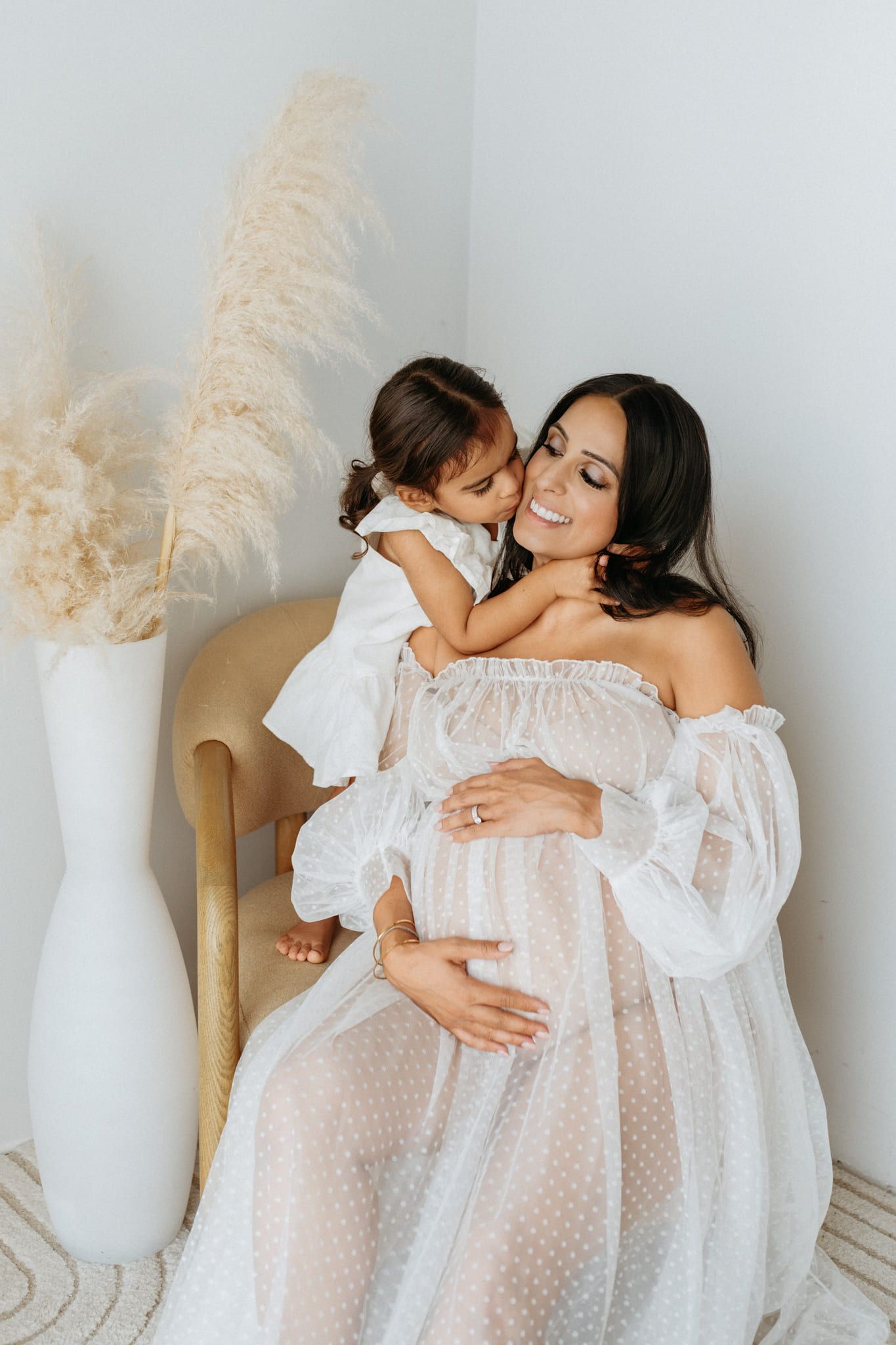 Family maternity photos studio session, expectant mother with her little daughter in a light studio