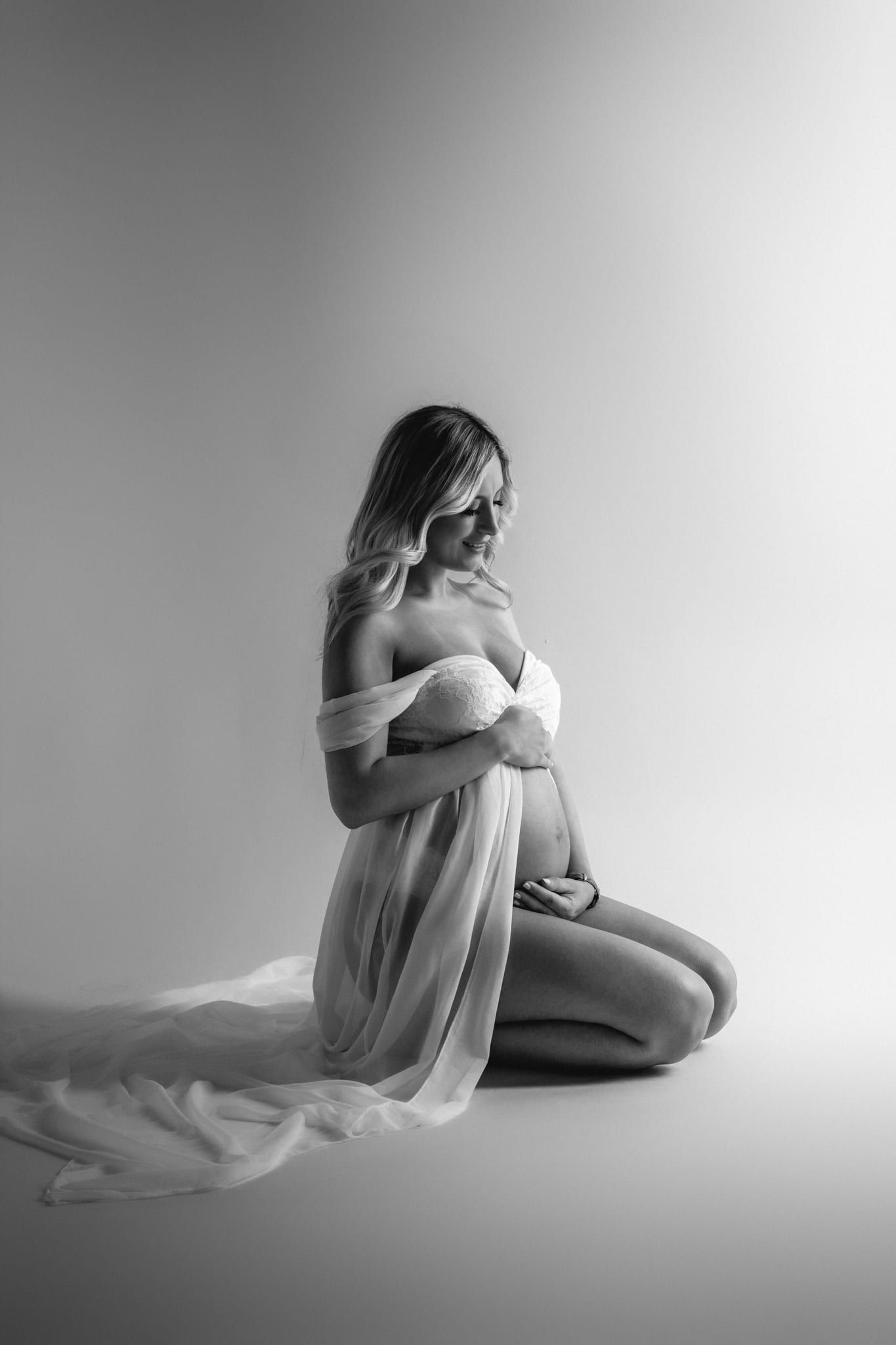 Pregnancy studio shoot, mom-to-be kneeling in a flowing gown, in black and white