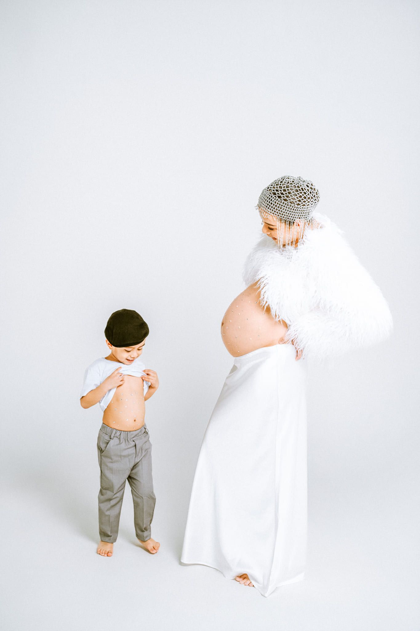 Maternity and family photography in a bright studio, little boy looking at his pregnant mom in a white gown
