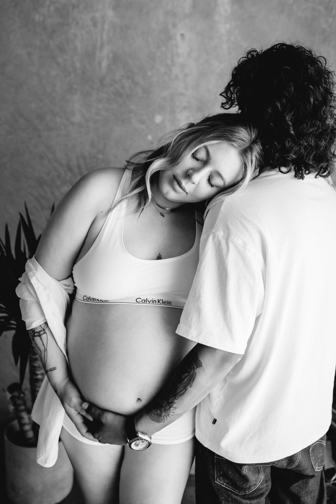Black and white pregnancy shoot in a studio, expecting couple leaning into each other