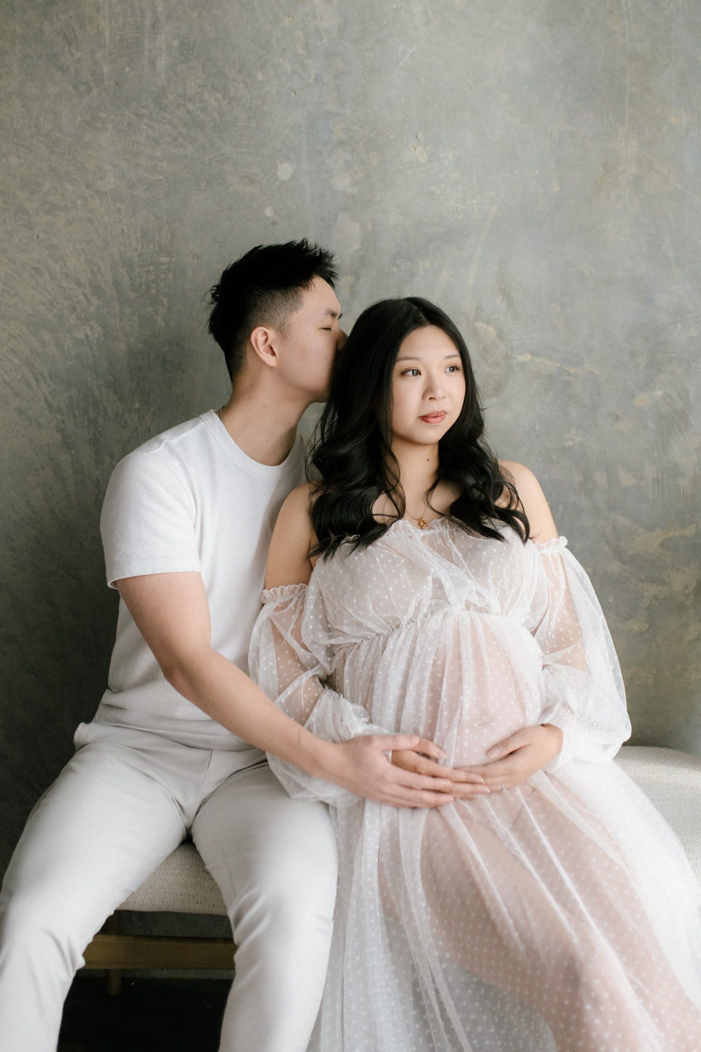 Creative studio maternity photoshoot, expectant mother in a sheer tulle gown in soft studio light