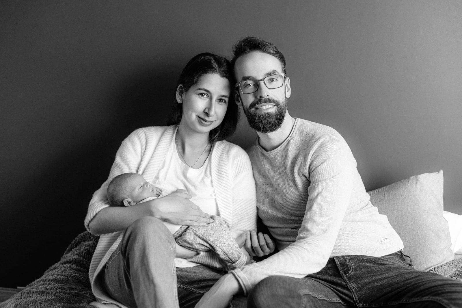 Newborn photography studio session, parents holding their newborn on a sofa in a studio, in black and white