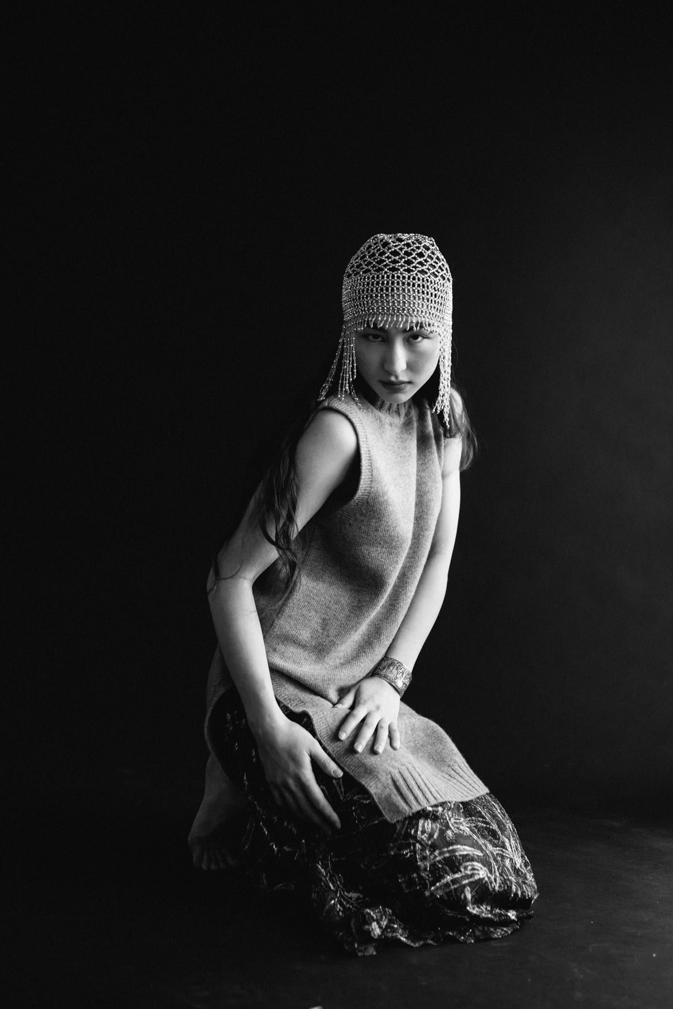 Black and white portrait photography, girl in a knit cap kneeling in a dark studio