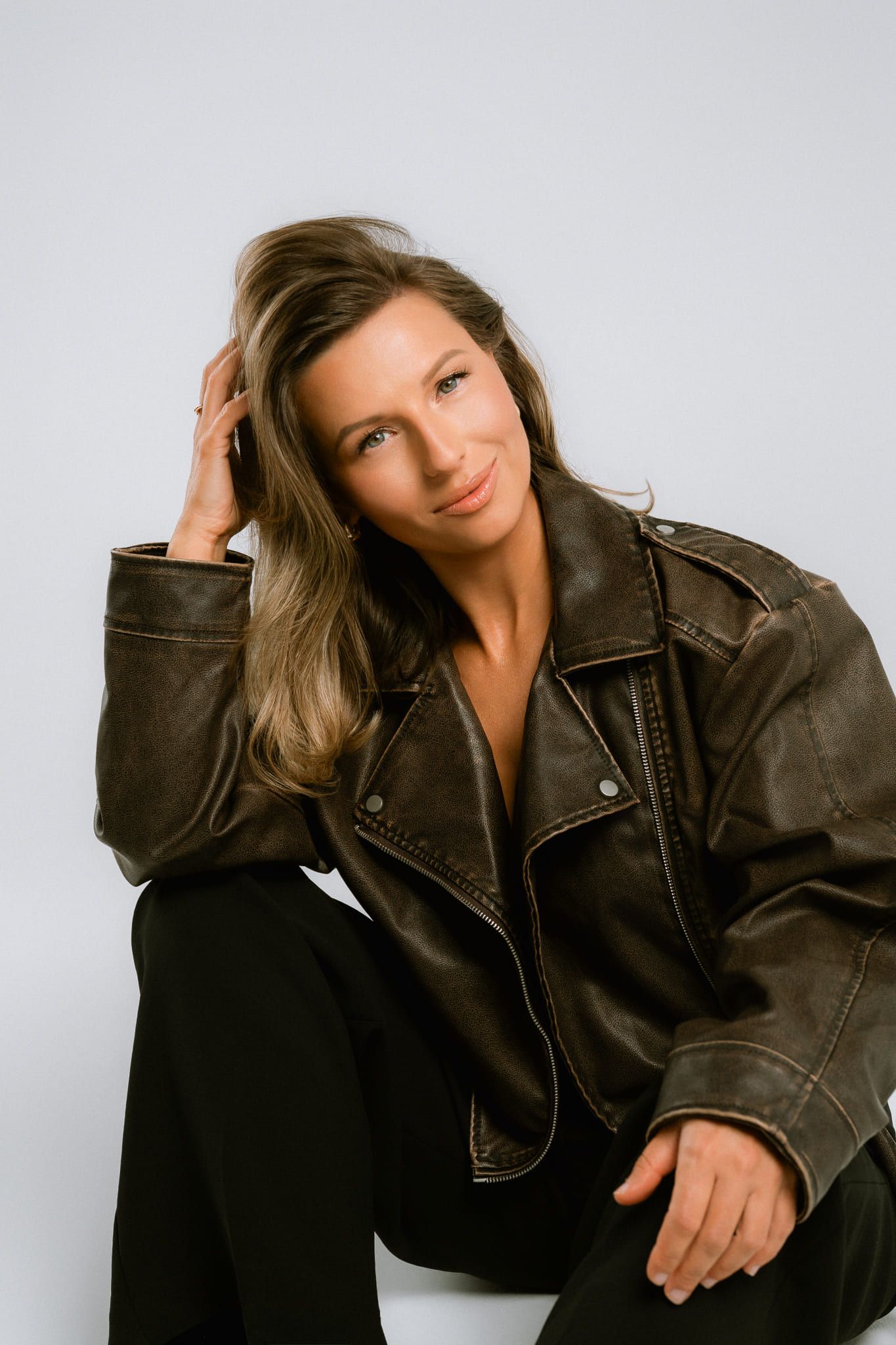 Portrait studio photoshoot, woman in a leather jacket sitting in a white studio