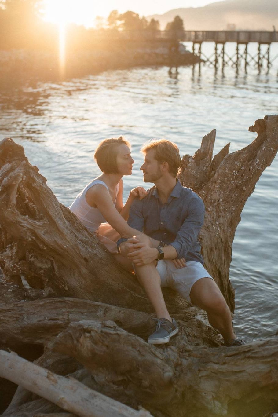 Creative engagement photos by the water at sunset, couple sitting on driftwood