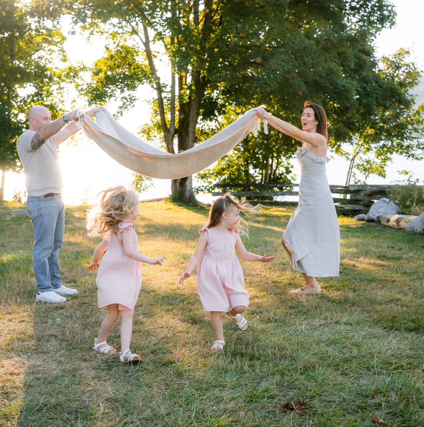 Langley family photographer, parents swinging a blanket over their two little girls on the grass at sunset