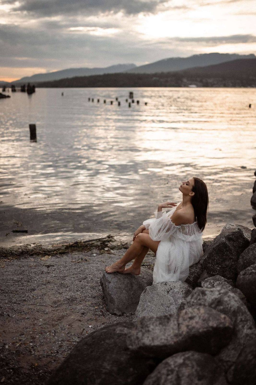 Professional branding photography at sunset, woman in white sitting on rocks by the sea