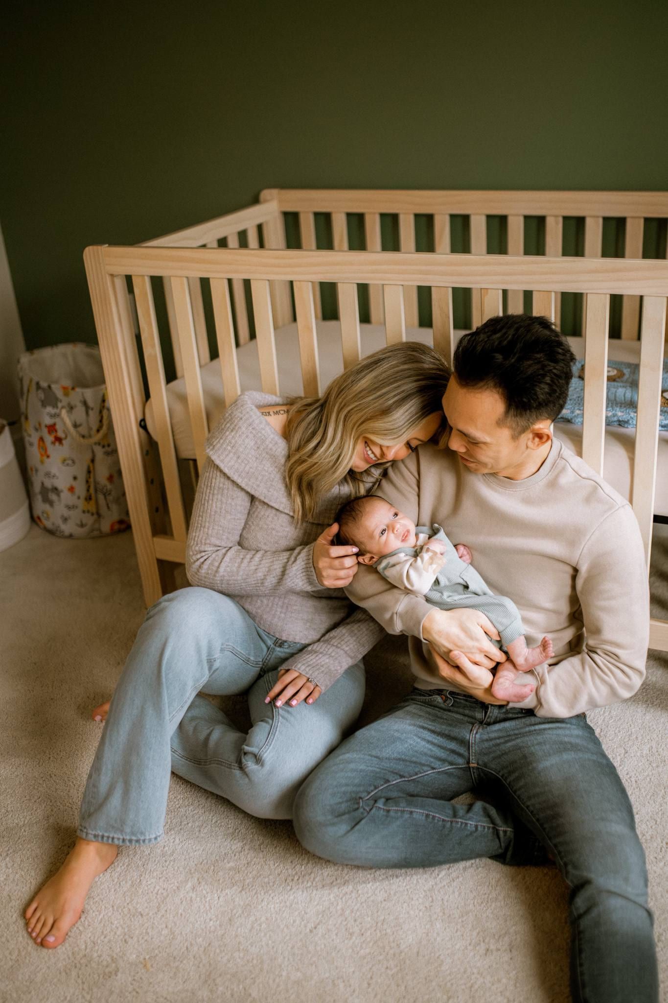 Parents seated beside a wooden crib holding their newborn