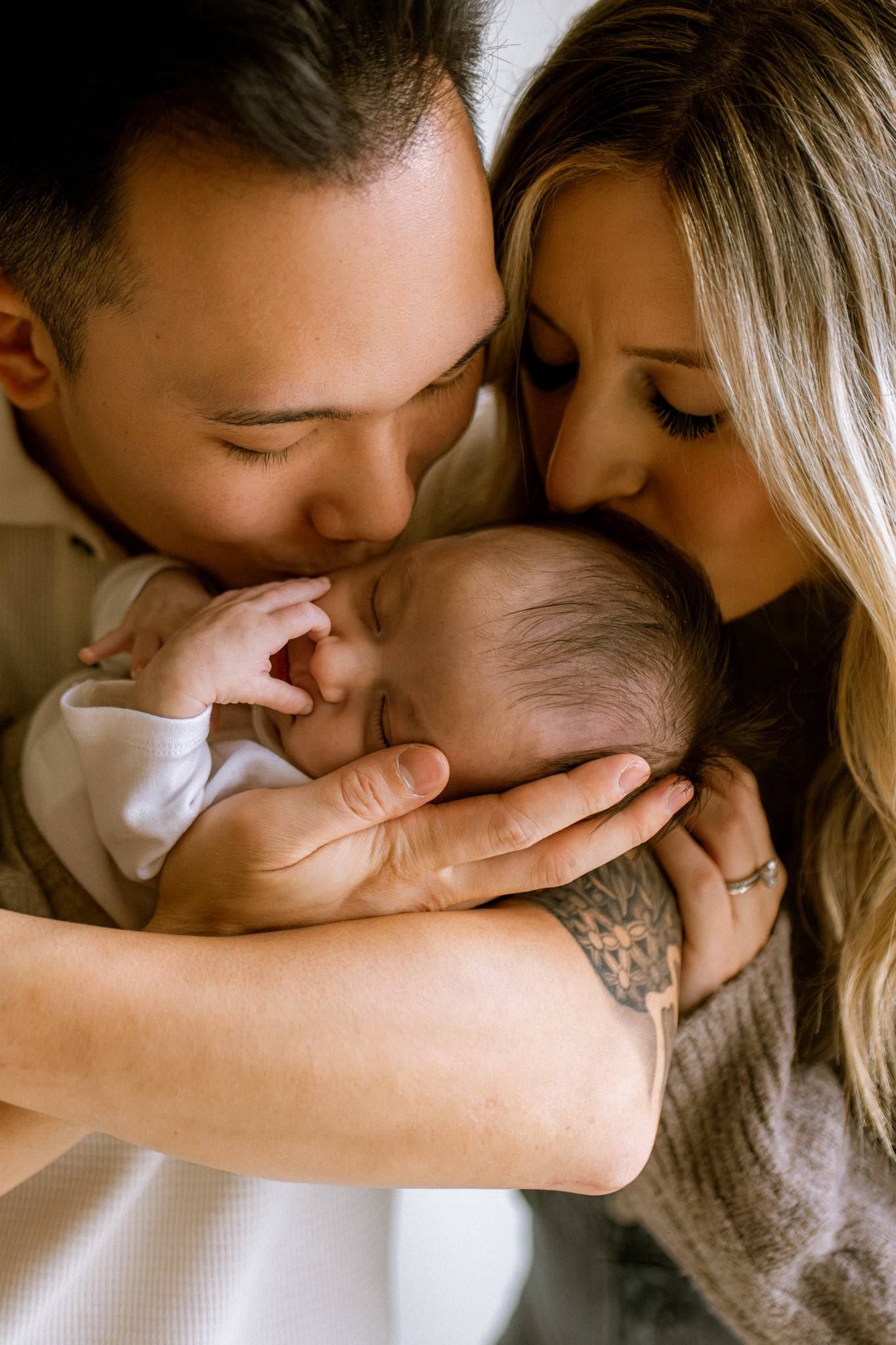 Parents kissing their newborn's head from either side