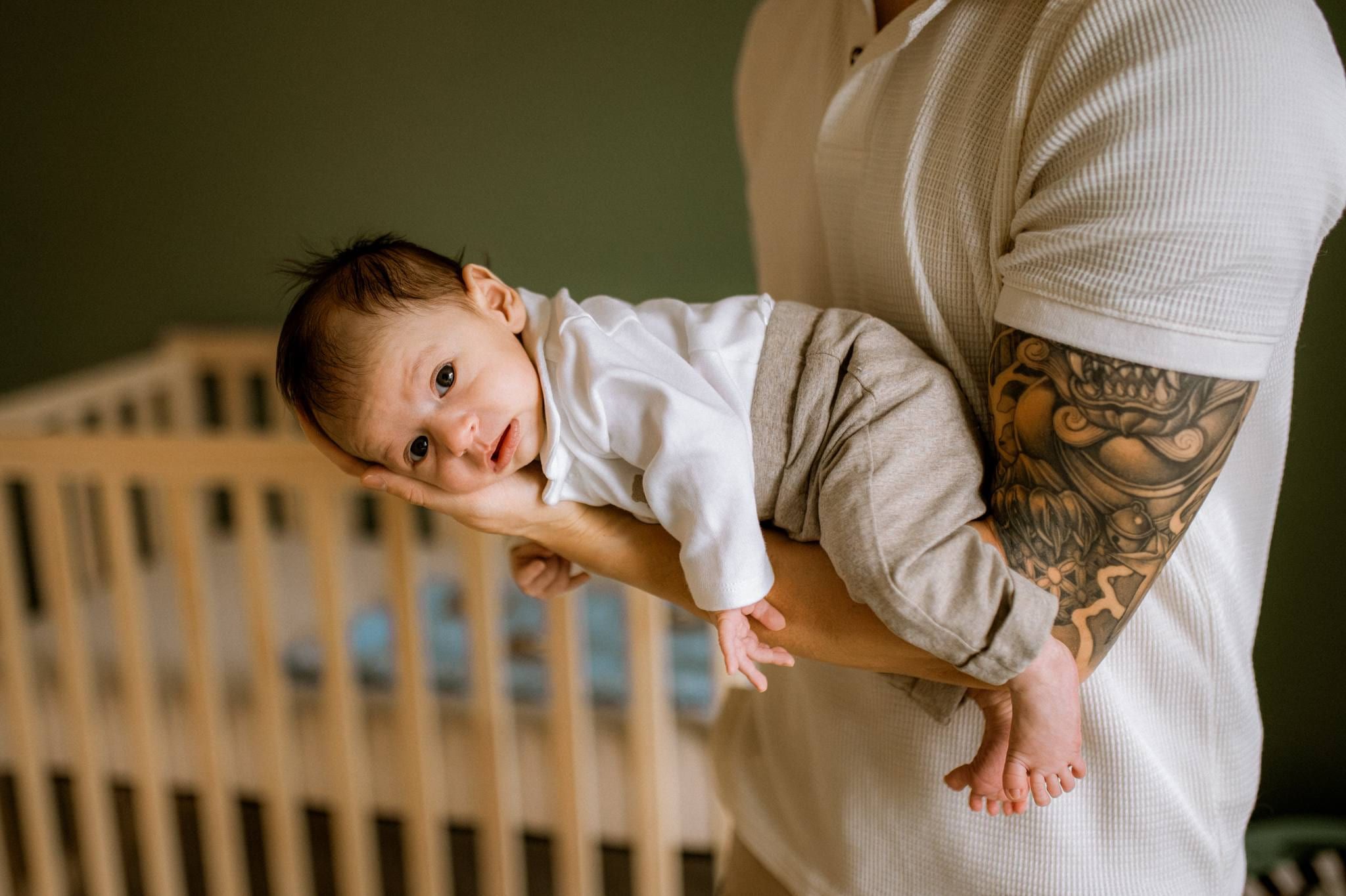 Father lifting his newborn beside the crib, the baby's eyes wide open