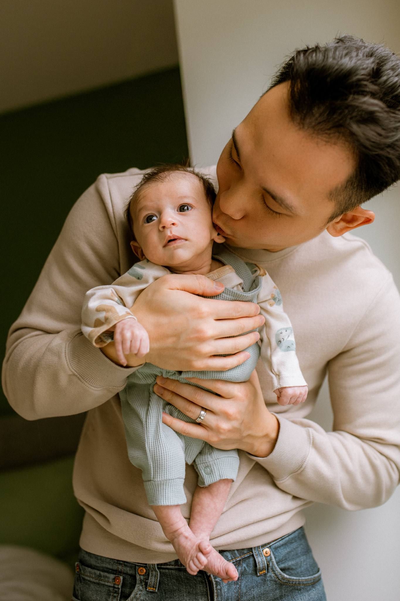 Father kissing his newborn cradled against his chest