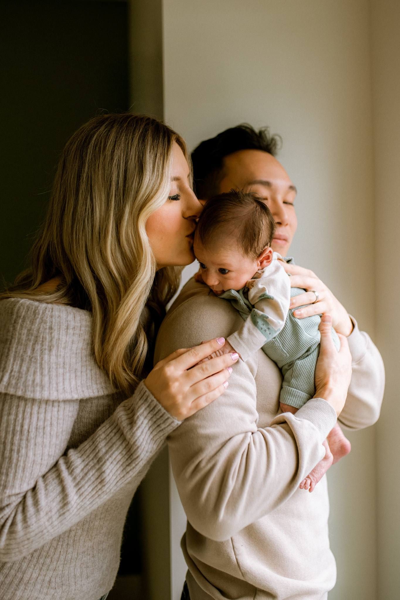 Parents kissing their newborn's head as they hold him together