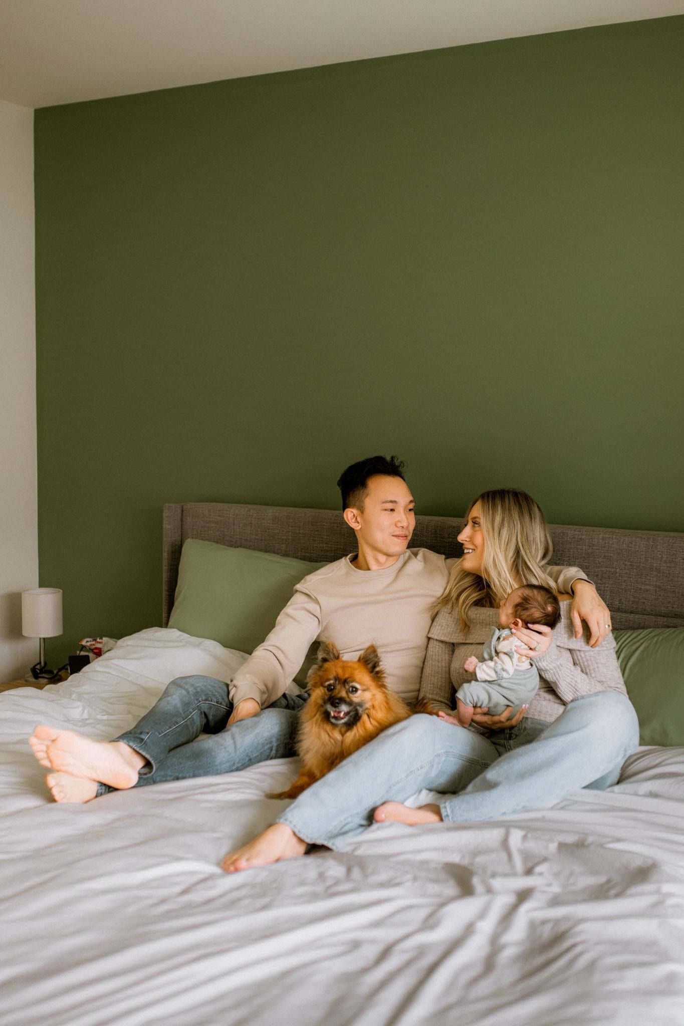 Family of three with their dog on the bed in a green bedroom
