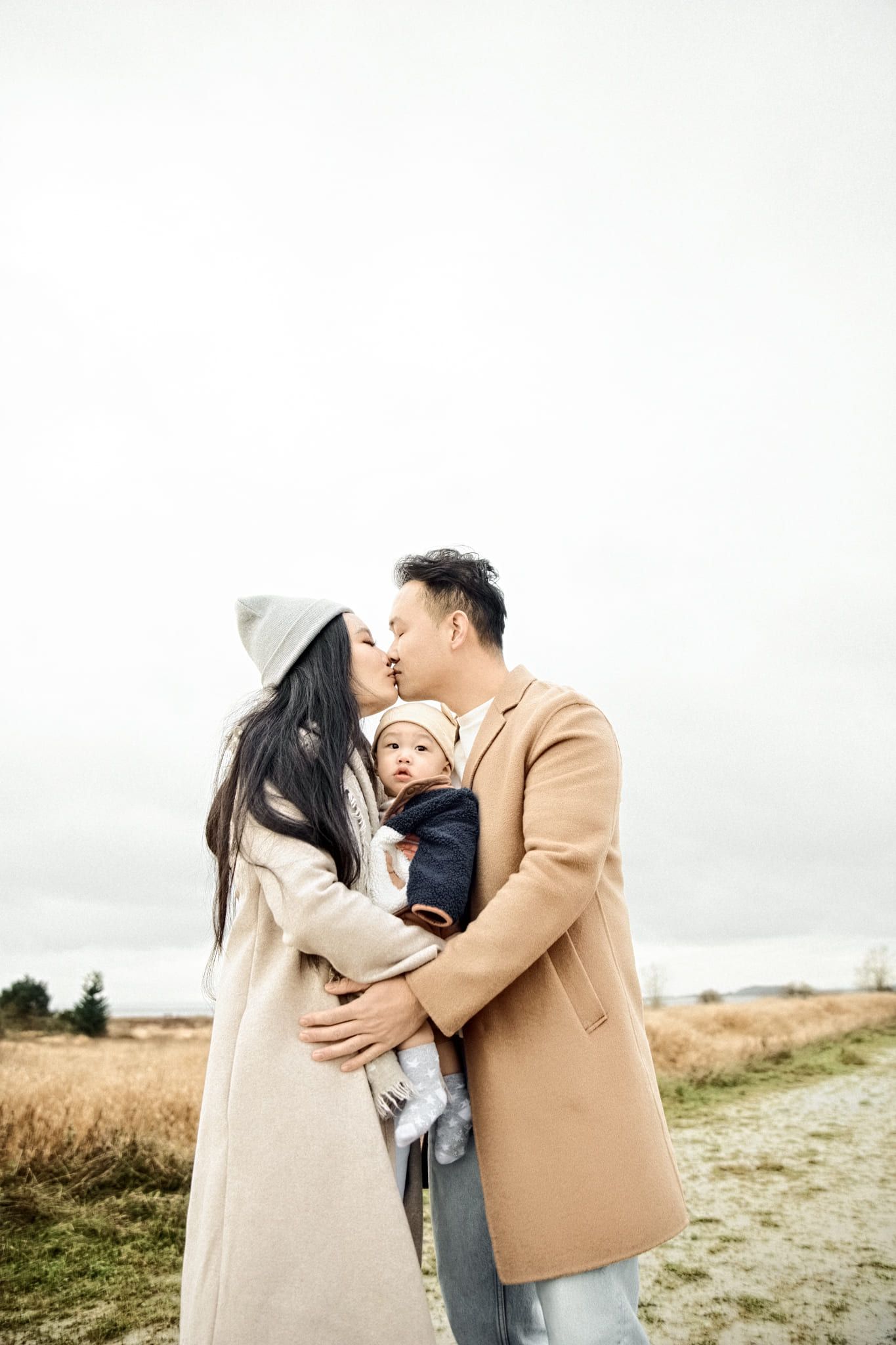 Mother kissing father as he holds their baby on a windswept path