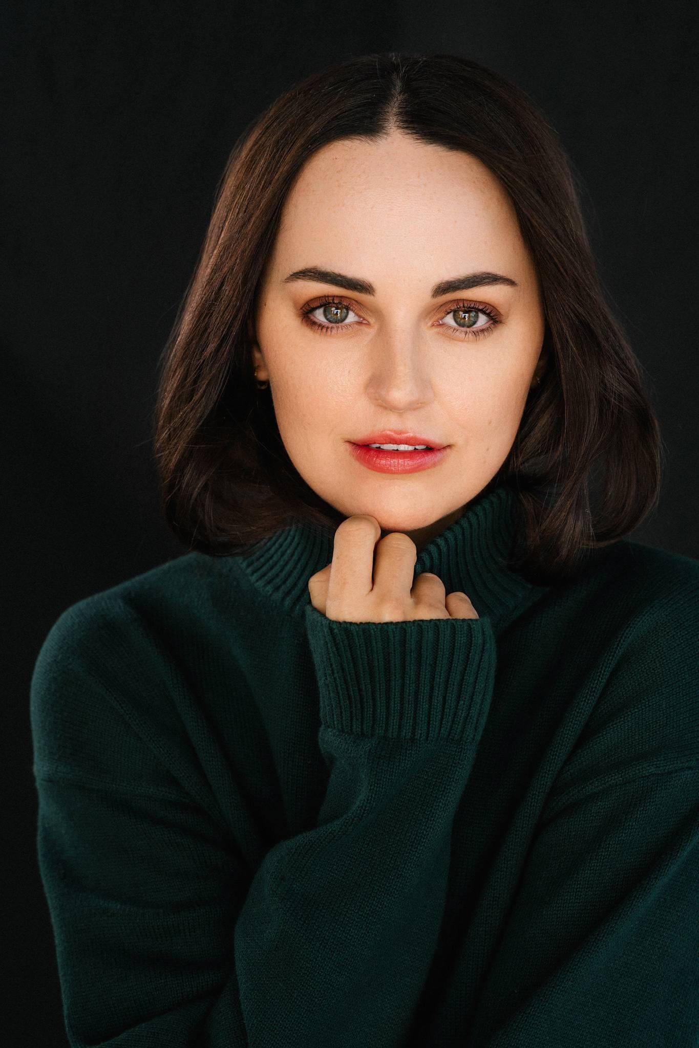 Woman in a green turtleneck sweater on a dark backdrop