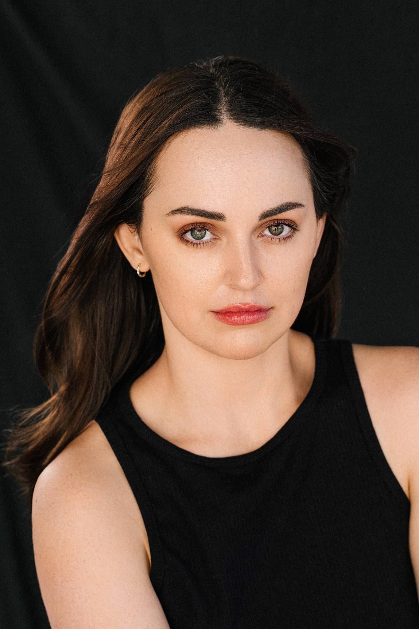 Woman in a black dress on a dark backdrop, hair swept to one side