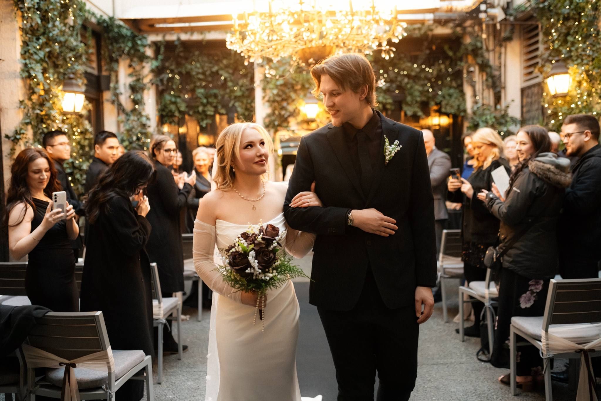 Viktoria and Josh walking arm in arm back down the aisle through the ivy-covered courtyard