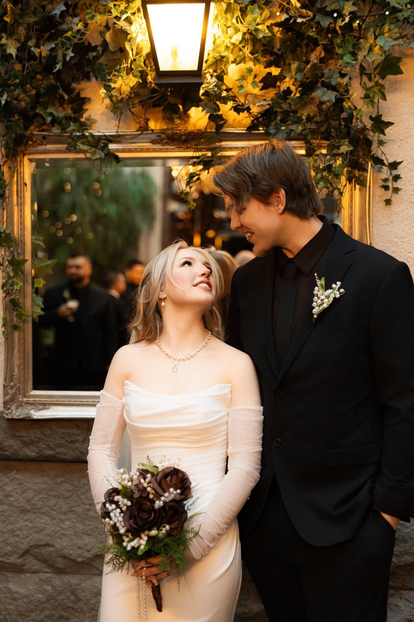Bride in a fur wrap holding a dark bouquet beside the groom under a lantern