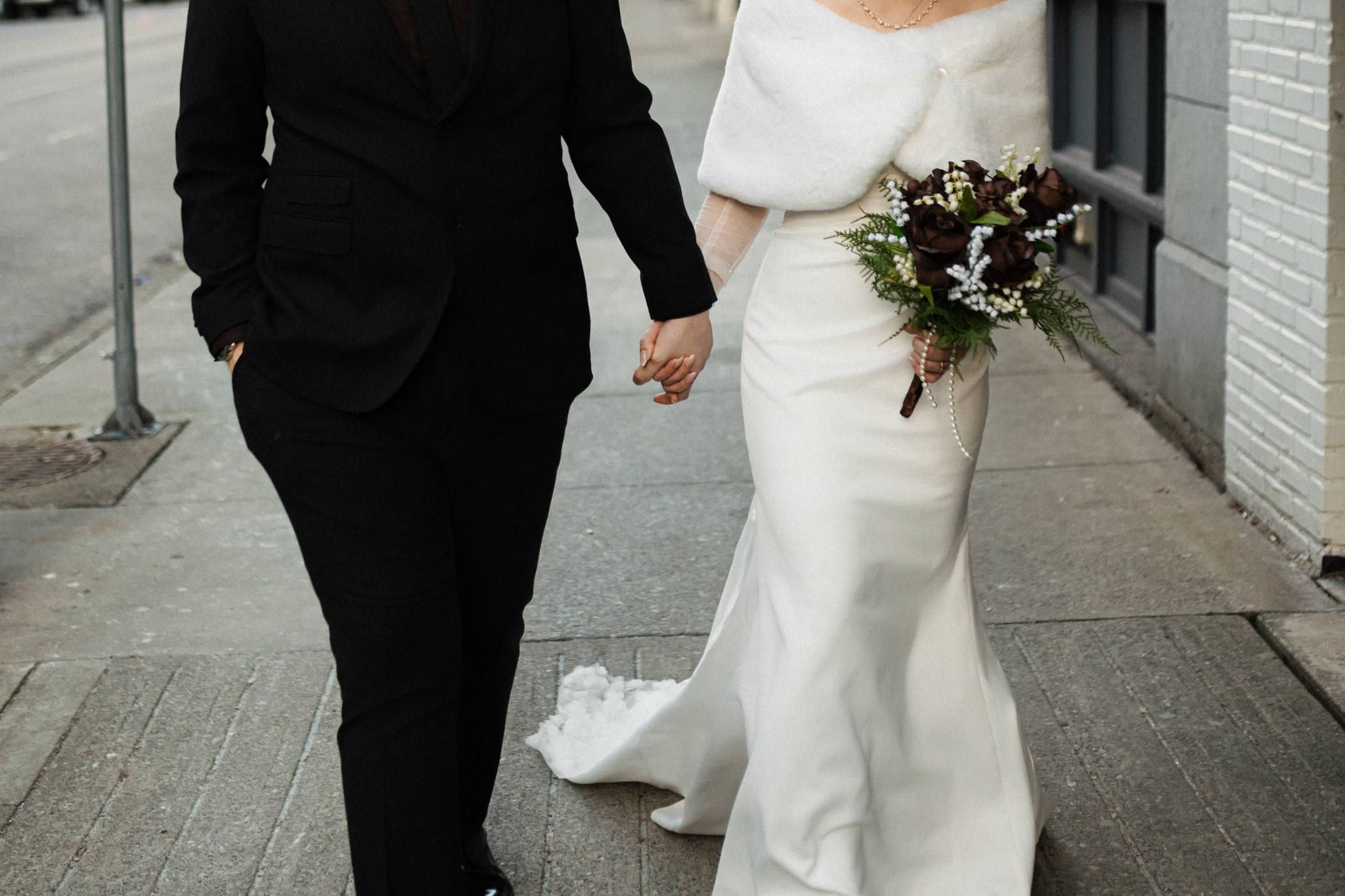 Bride in a fur wrap walking down the sidewalk with her bouquet