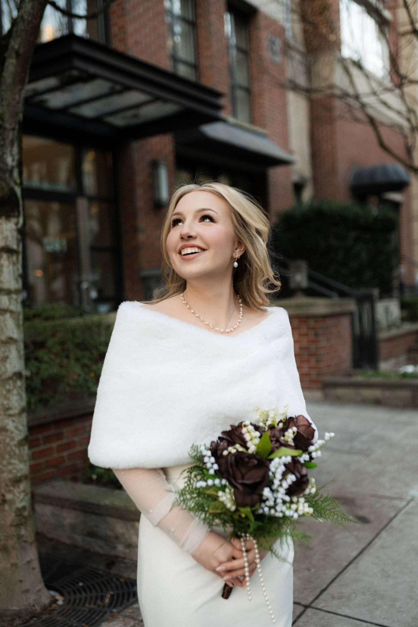 Bride in a fur wrap smiling with her bouquet on the city street