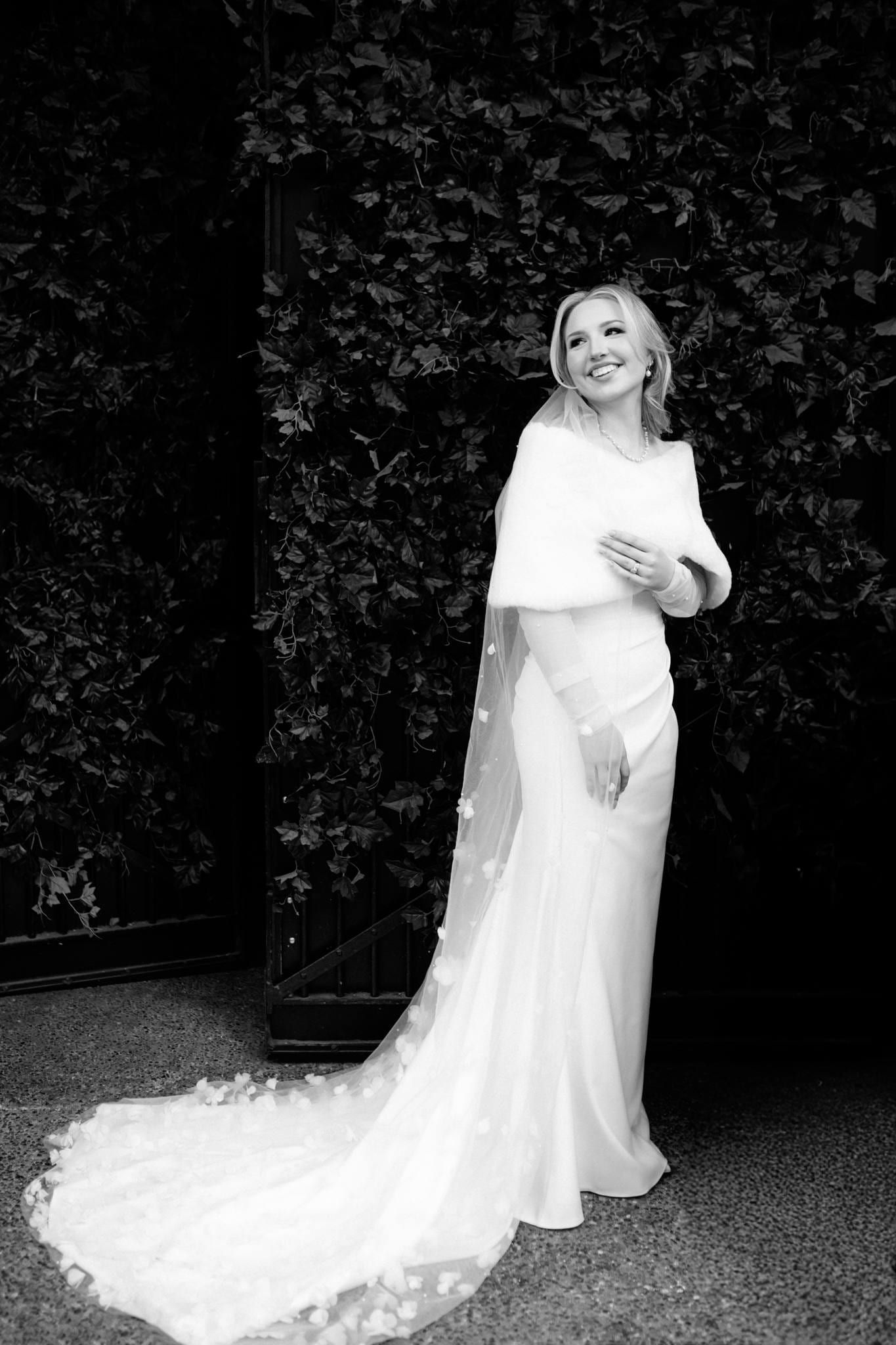 Bride in a fur wrap before a dark green wall, train spread behind