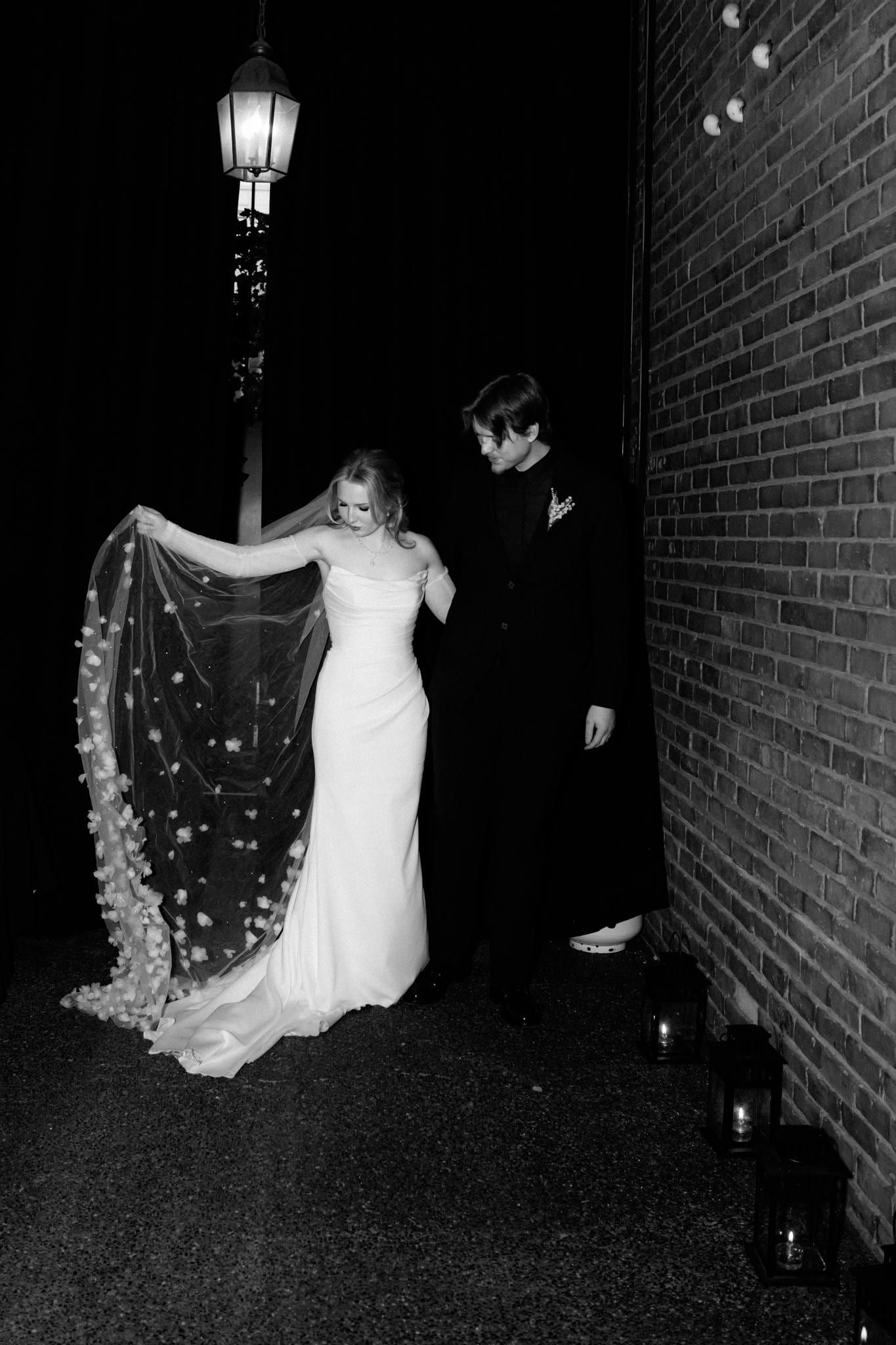 Bride in a fur wrap with her veil lifted under a street lamp at night