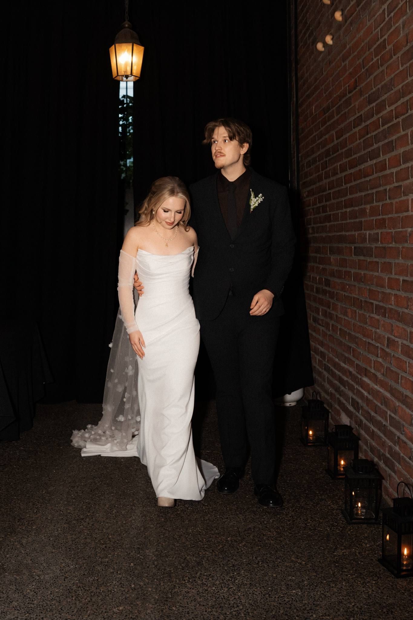 Bride and groom walking through a candlelit courtyard under a street lamp